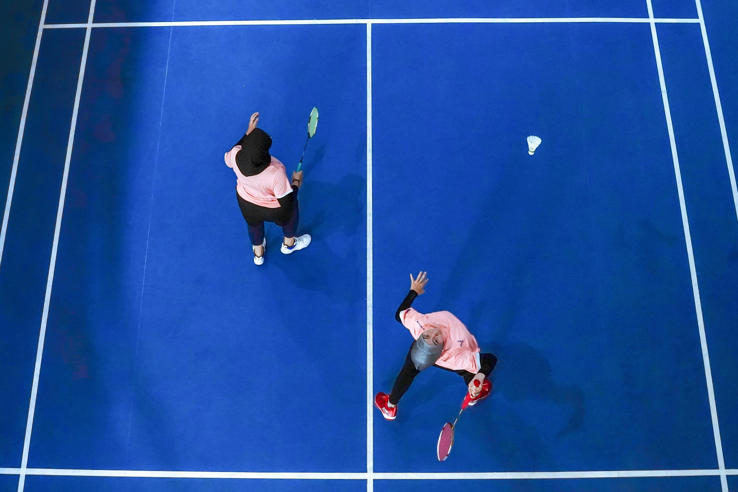 Top view of two women playing badminton on a blue court in Jakarta, Indonesia.