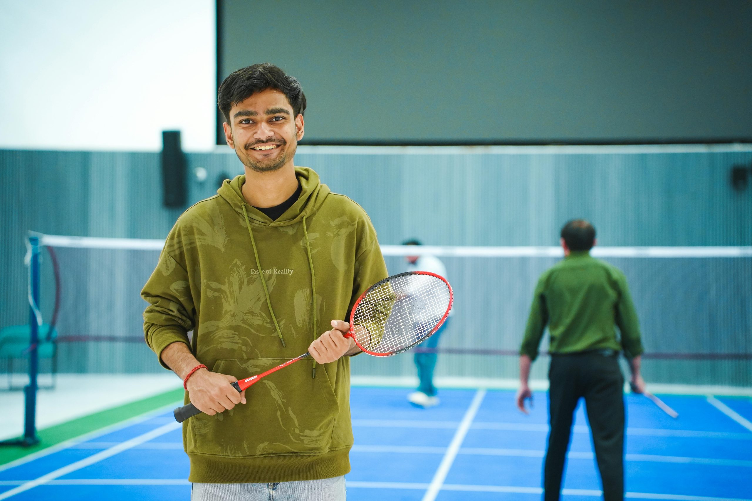 Portrait of a young man holding a badminton racket indoors, ready to play.