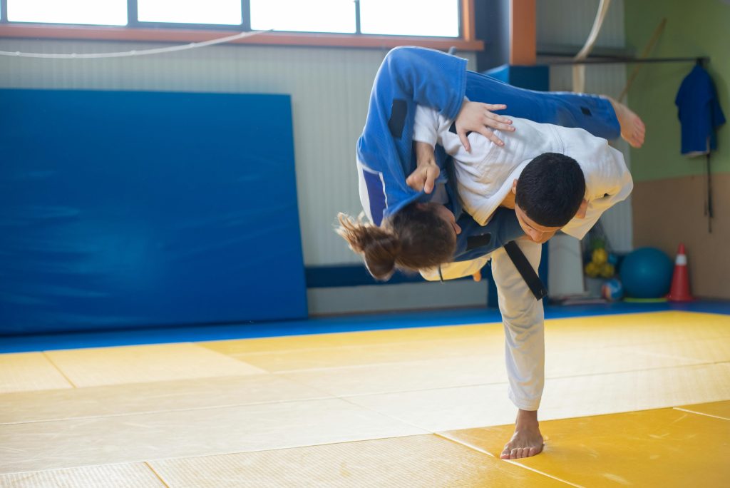 Two judokas practicing a powerful throw during judo training indoors on tatami mats.